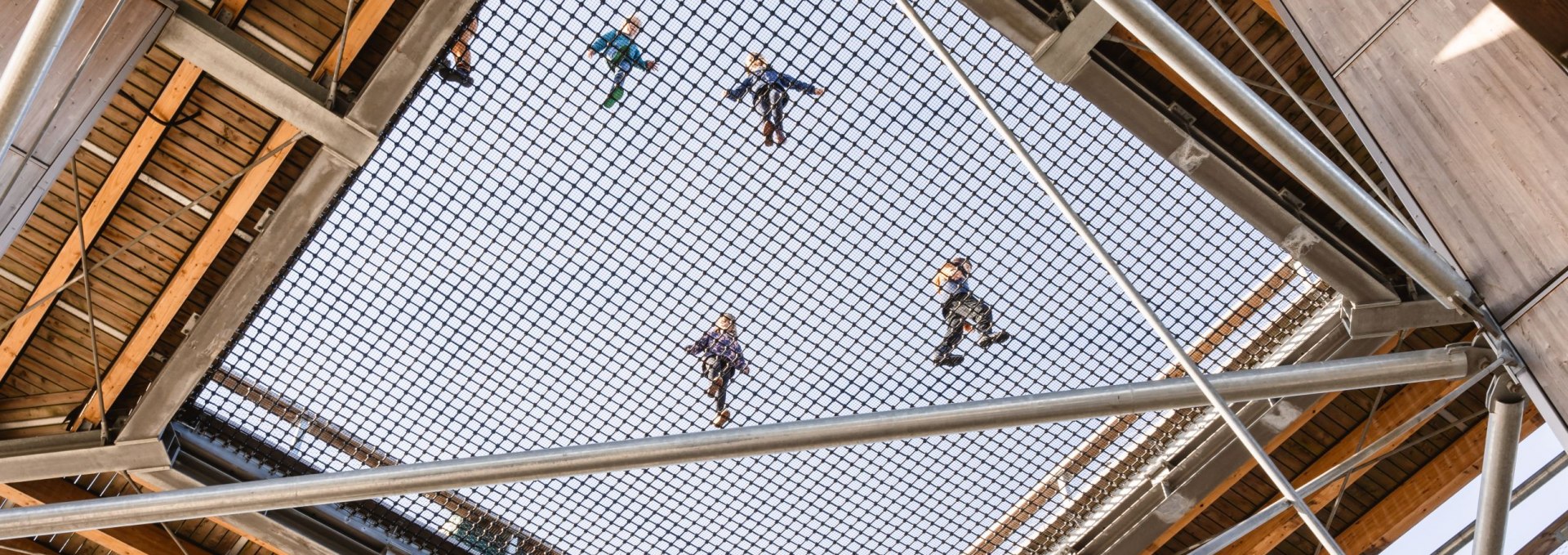 Blick von unten durch ein gro&szlig;es Sicherheitsnetz in einem Holzturm, auf dem mehrere Kinder stehen und spielen.