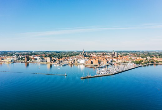 Luftaufnahme der Hansestadt Stralsund mit Hafen, historischer Altstadt und Ostsee bei blauem Himmel.
