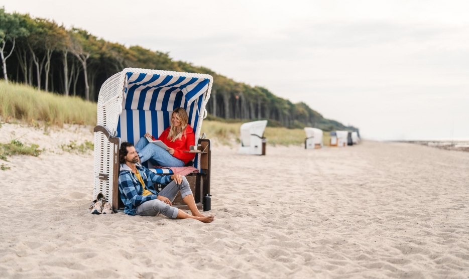 P&auml;rchen sitzt in einem Strandkorb am Strand von Graal-M&uuml;ritz an der Ostseek&uuml;ste. Im Hintergrund ist der K&uuml;stenwald zu sehen.