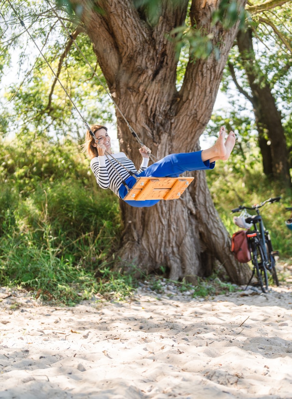 Eine Frau schaukelt am Strand unter einem Baum in der N&auml;he von Lubmin.
