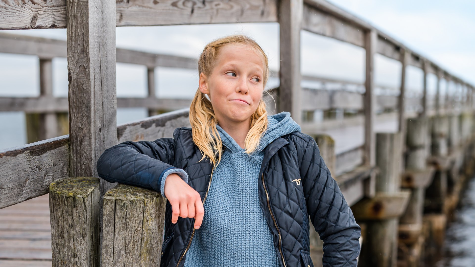 Portrait Madita von Klitzing lehnt sich am Strand an das Holz der Seebr&uuml;cke in Zingst mit der Ostsee im Hintergrund.