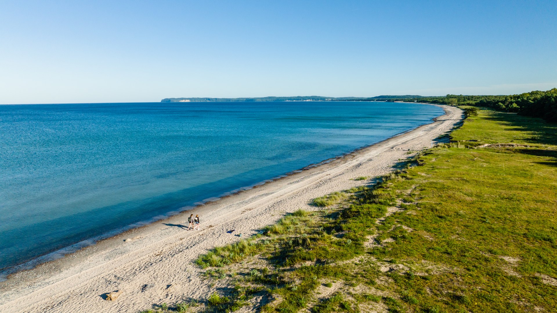 Das Ziel der Wanderung ist erreicht: Der Naturstrand bei Mukran erstreckt sich mehrere Kilometer entlang der Ostseeküste von Rügen., © TMV/Gänsicke Zwei Frauen wandern am Naturstrand von Mukran. Blick aus der Luft mit der Ostsee im Hintergrund.