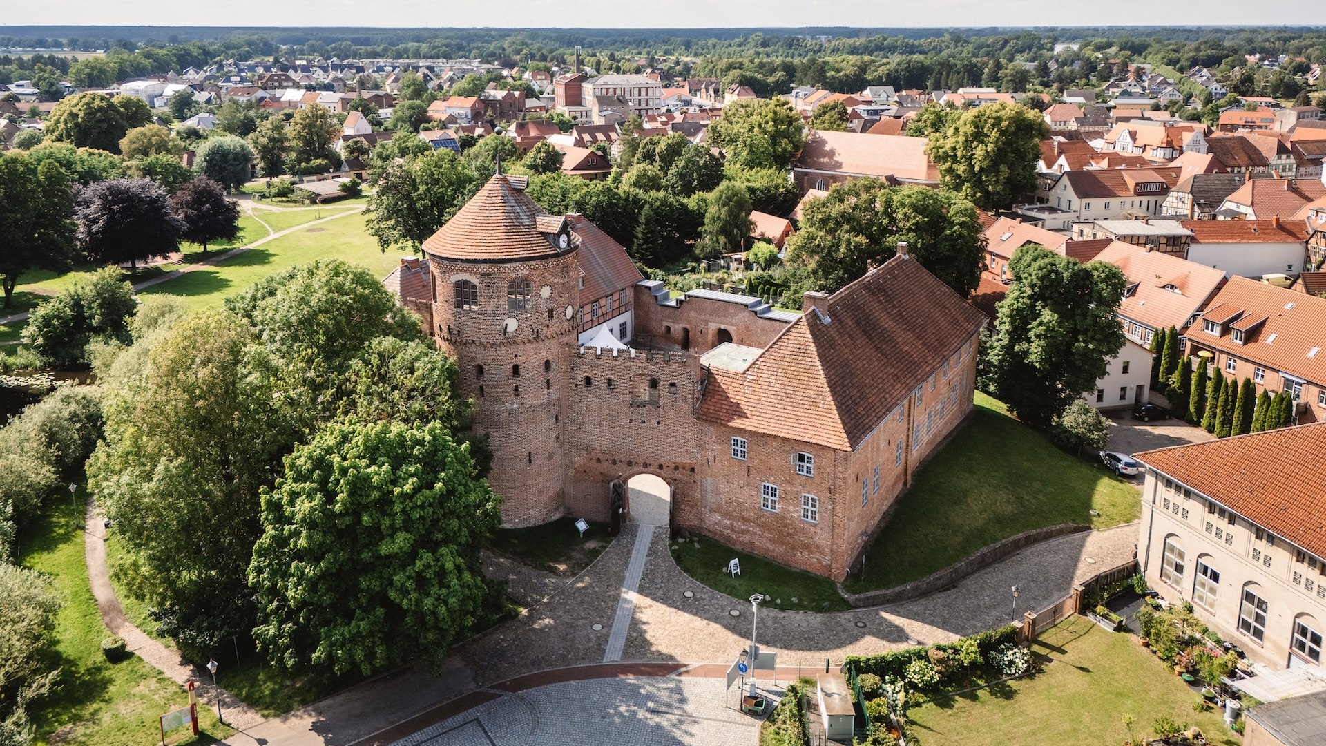 Eine Luftaufnahme der historischen Burg Neustadt-Glewe, umgeben von gr&uuml;nen B&auml;umen und der malerischen Altstadt mit roten Ziegeld&auml;chern.