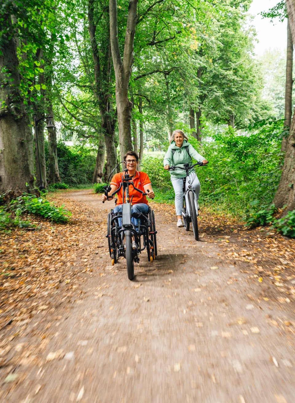 Elektrisches Handbike und Fahrradfahrerin auf einem Waldweg unterwegs.