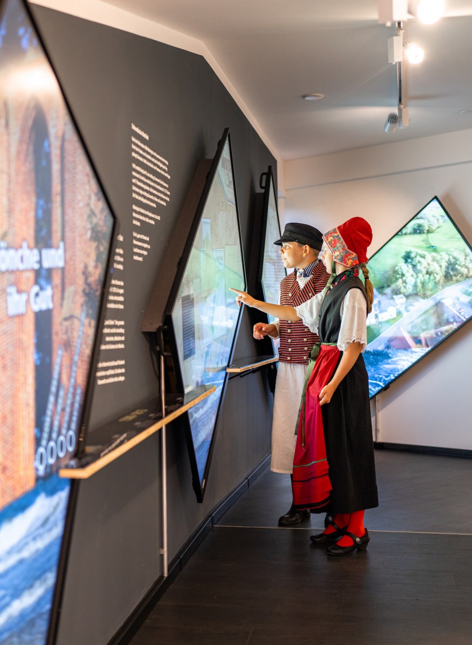 Kinder stehen in traditioneller Tracht vom Mönchgut im Museum und schauen sich die Ausstellung an. // Mönchguter Trachten sind manchmal auch heute an Festtagen auf Rügen zu sehen - und natürlich in der ständigen Ausstellung des Museums // © MV-T/Gross Kinder stehen in traditioneller Tracht vom Mönchgut im Museum und schauen sich die Ausstellung an.