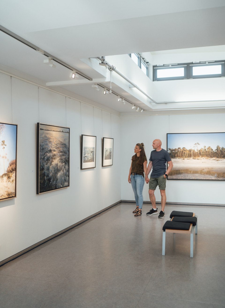 Ein Paar schlendert durch eine Galerie. An den W&auml;nden h&auml;ngen Naturfotografien.