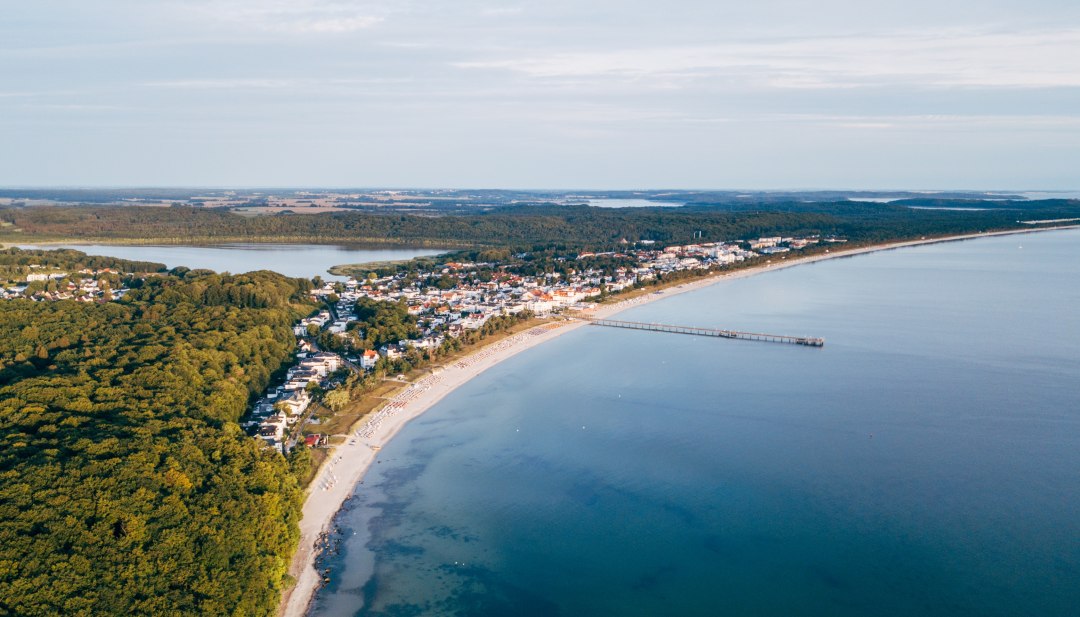Luftaufnahme von Binz auf R&uuml;gen mit Seebr&uuml;cke, K&uuml;stenlinie und umliegenden W&auml;ldern.