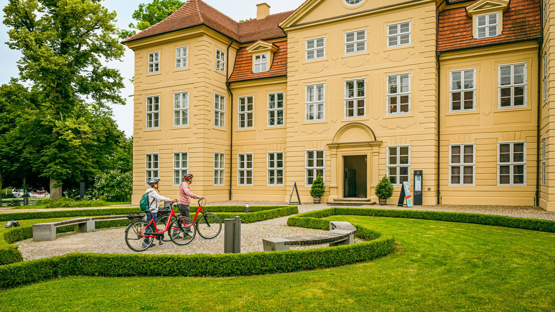 Royaler Schlusspunkt der Radtour ist Schloss Mirow., © TMV/Tiemann Vor dem Schloss Mirow steht ein Paar mit E-Bikes