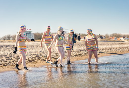 Eisbader gehen am Strand von Warnemünde in die Ostsee bei Sonnenschein.