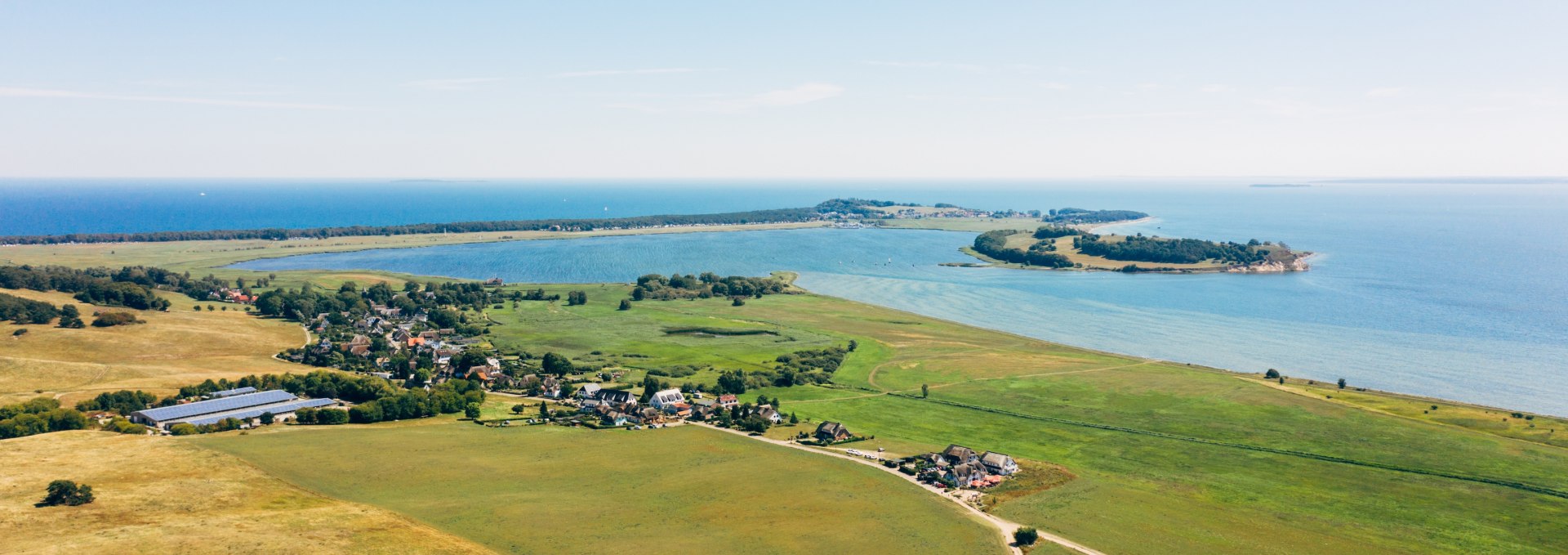 Luftaufnahme der Zicker Berge auf der Halbinsel Mönchgut mit weiten Wiesen, kleinen Dörfern und Blick auf die Ostsee und umliegende Halbinseln unter klarem Himmel. // Ein Blick über die malerischen Zicker Berge auf der Halbinsel Mönchgut: Weite Wiesen, charmante Dörfer und die schimmernde Ostsee machen diesen Ort zu einem Paradies für Naturliebhaber. // © MV-T/Friedrich Luftaufnahme der Zicker Berge auf der Halbinsel Mönchgut mit weiten Wiesen, kleinen Dörfern und Blick auf die Ostsee und umliegende Halbinseln unter klarem Himmel.
