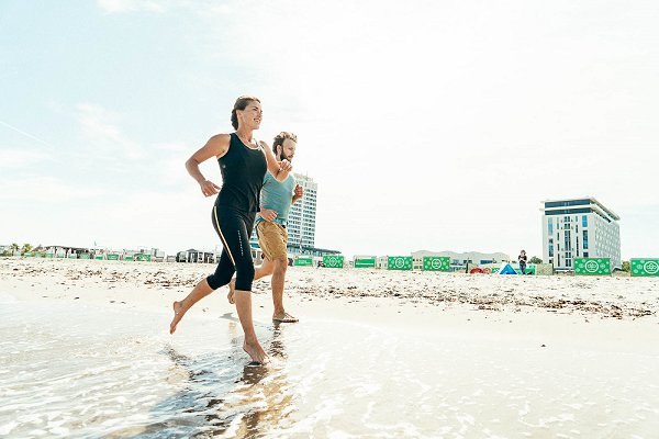 Eine Sportlerin und ein Sportler laufen am Strand von Warnem&uuml;nde im Sommer