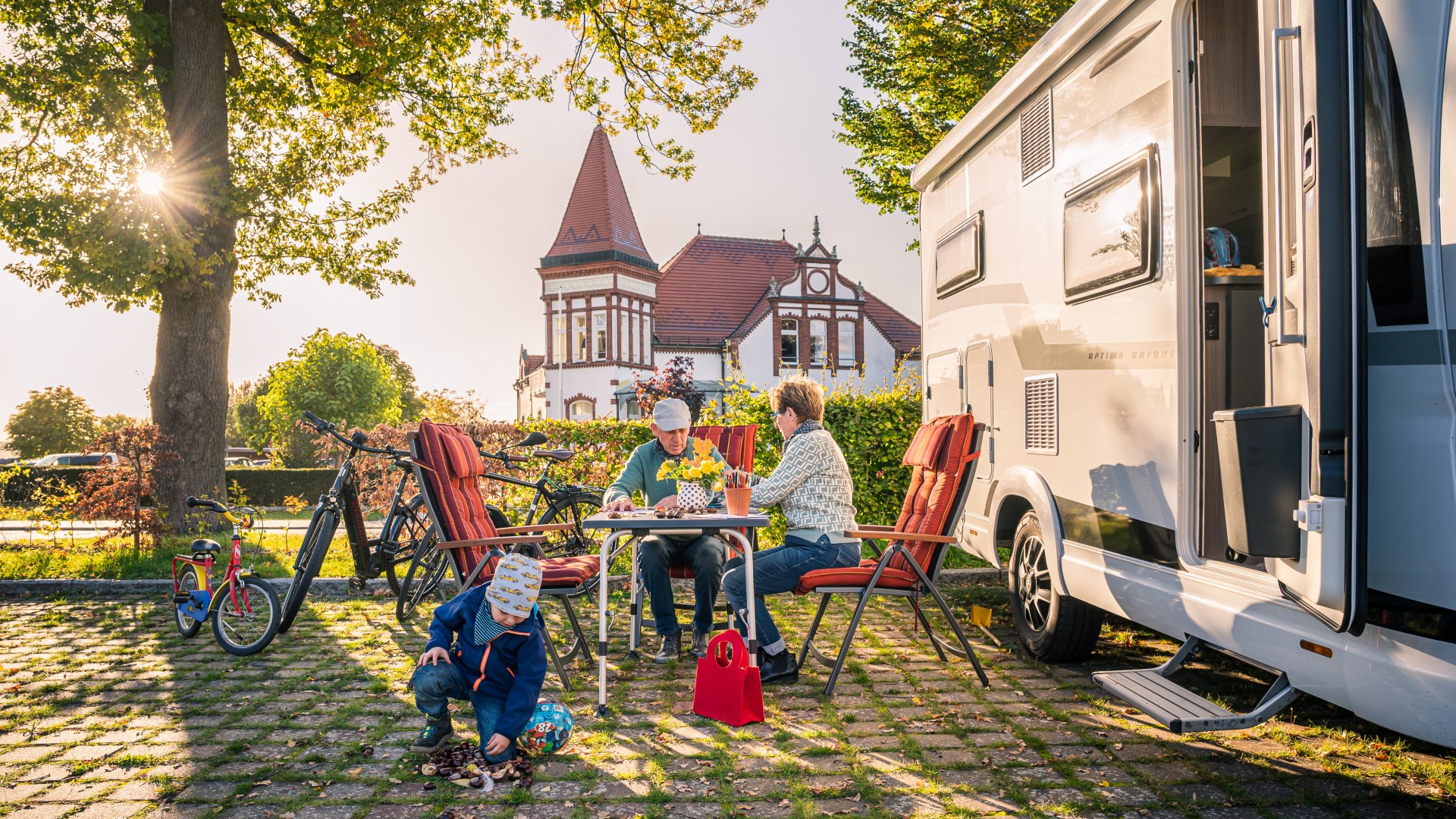 Oma, Opa und Enkel vor dem Reisemobil auf dem Stellplatz am Stadthafen in Neustrelitz bei Sonnenuntergang