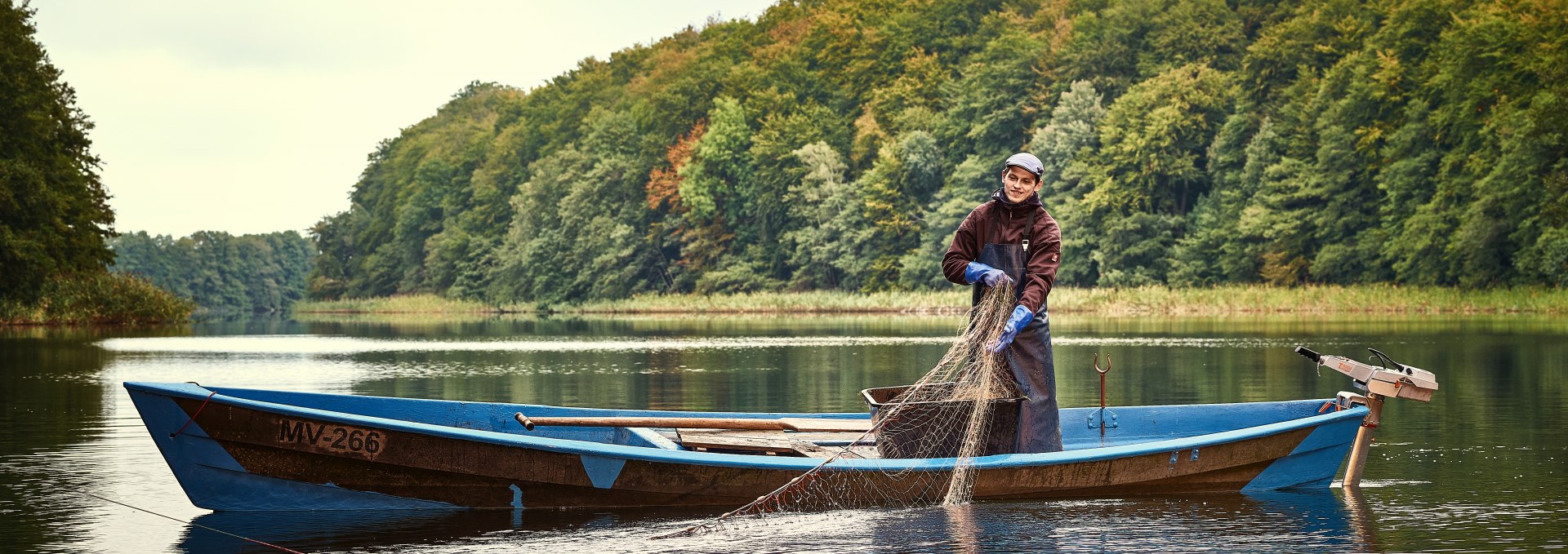Fischer in der Mecklenburgischen Seenplatte zieht gerade seine Netze ein auf das Boot.