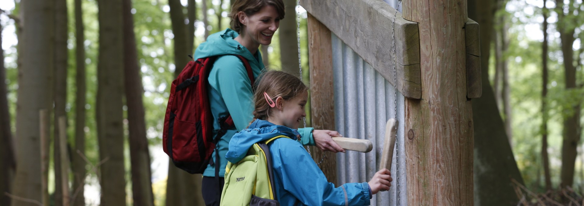 Eine Mutter und ihre Tochter stehen vor einer Installation mit Klangröhren im Klangwald von Graal-Müritz. Beide halten Holzklöppel und schlagen die Röhren an, um Töne zu erzeugen, während sie lächeln. // Interaktive Klangerlebnisse im Klangwald von Graal-Müritz – Mutter und Tochter erzeugen gemeinsam Töne mit den Klangröhren. // © Lars Schneider / schneider outdoor visions Eine Mutter und ihre Tochter stehen vor einer Installation mit Klangröhren im Klangwald von Graal-Müritz. Beide halten Holzklöppel und schlagen die Röhren an, um Töne zu erzeugen, während sie lächeln.