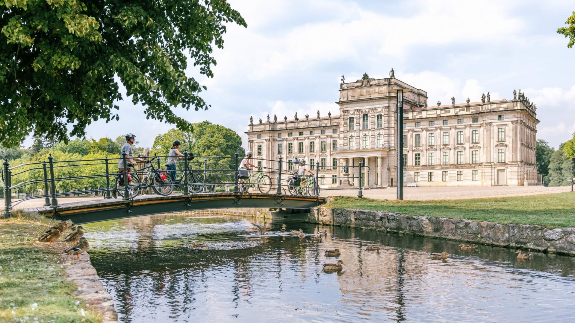 Das Schloss Ludwigslust mit Fahrradfahrern, die den Kanal auf einer Brücke überqueren.
