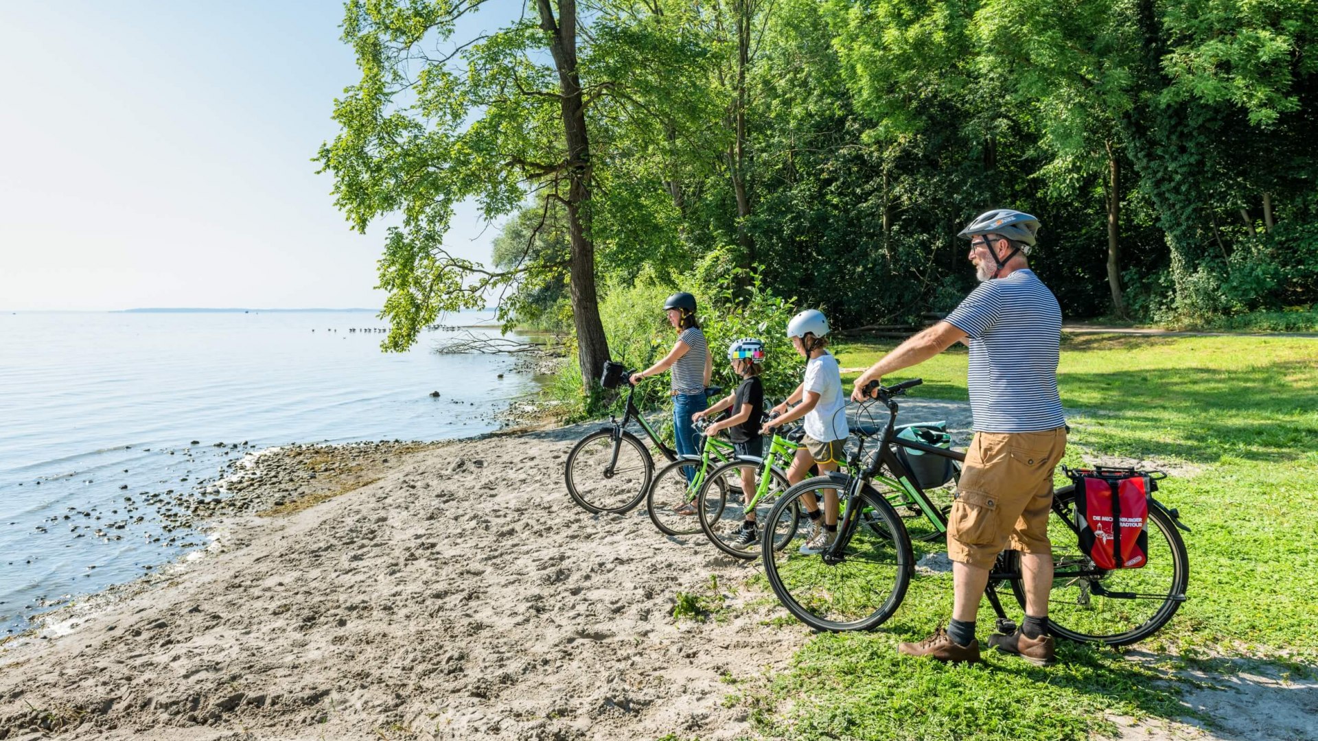 Eine Familie mit Fahrrädern steht an einer Badestelle am Plauer See // Erfrischung auch fürs Auge - Die vielen Gewässer in der Mecklenburgischen Seenplatte sind eine Wohltat für Körper und Seele. // © MV-T/Tiemann Eine Familie mit Fahrrädern steht an einer Badestelle am Plauer See