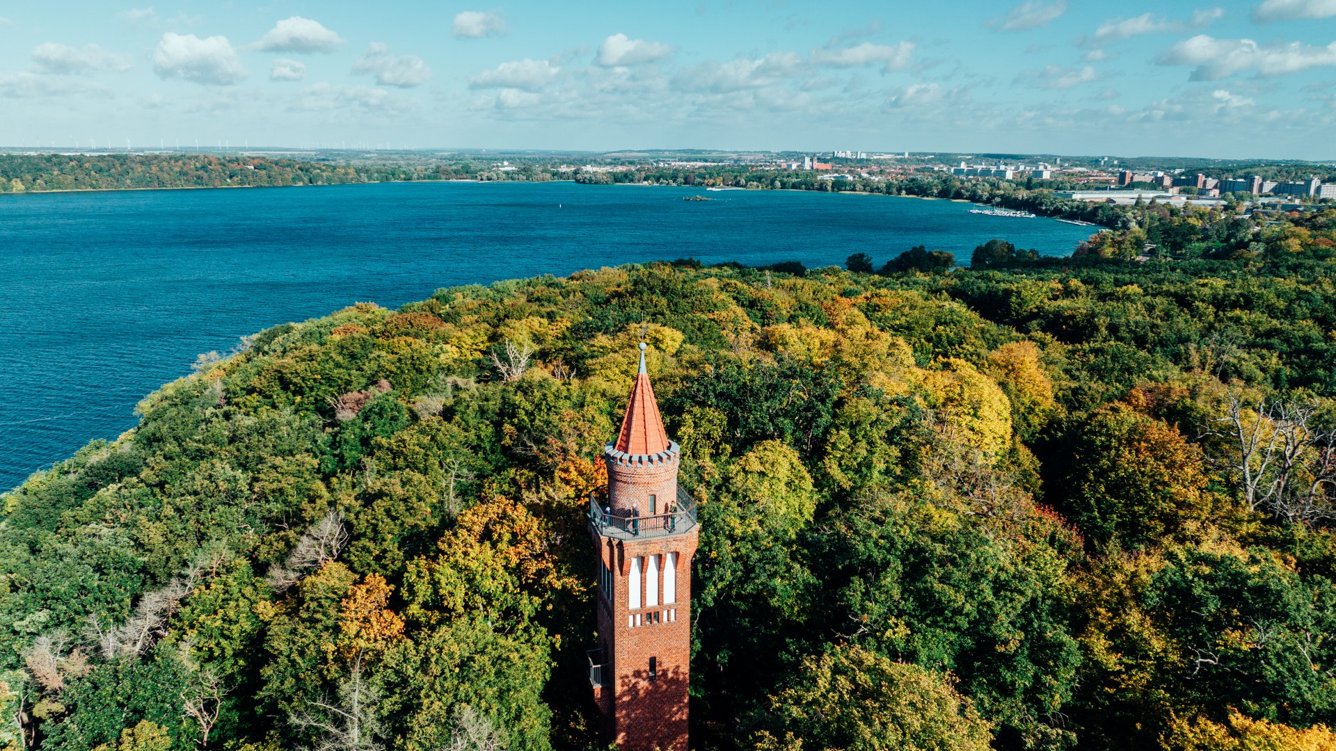 Das weite Panorama vom Aussichtsturm Behmshöhe am Tollensesee, der aus dem Wald hervorschaut und im Hintergrund der See.