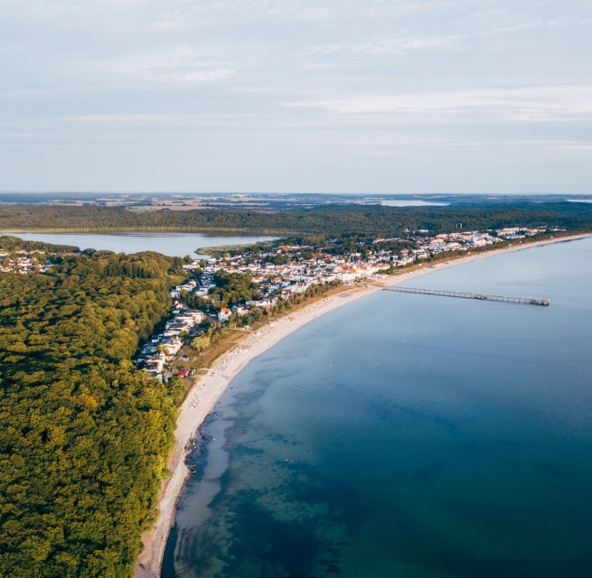 Luftaufnahme von Binz auf R&uuml;gen mit Seebr&uuml;cke, K&uuml;stenlinie und umliegenden W&auml;ldern.