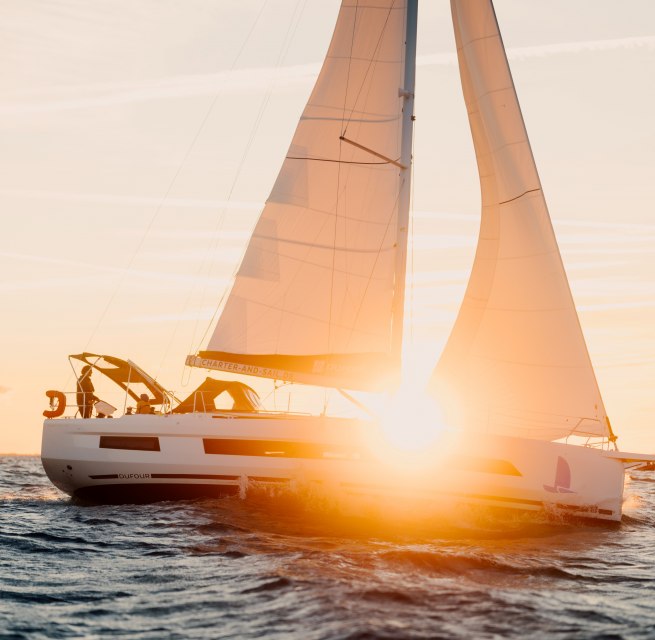 Segelboot mit orangefarbenen Segeln auf der Ostsee vor Warnem&uuml;nde bei Sonnenuntergang.