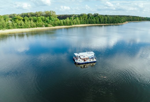 Mit dem Hausboot unterwegs auf der Mecklenburgischen Seenplatte, © TMV/Gänsicke Zwei Hausboote liegen nebeinander auf einem See und daneben schwimmt eine Person.