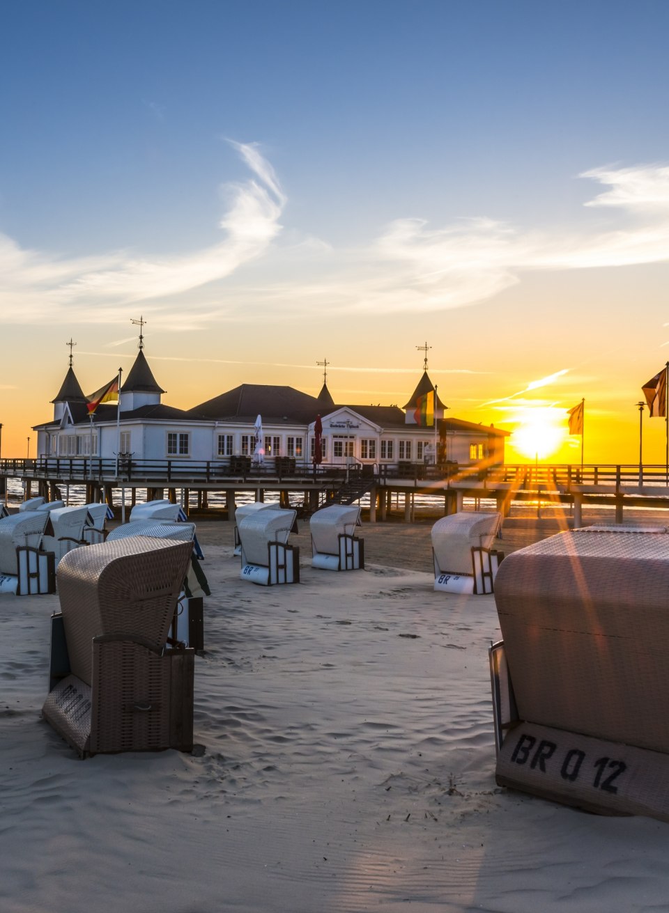 Sonnenaufgang an der Ahlbecker Seebr&uuml;cke mit Strandk&ouml;rben am Ostseestrand und goldener Morgensonne.
