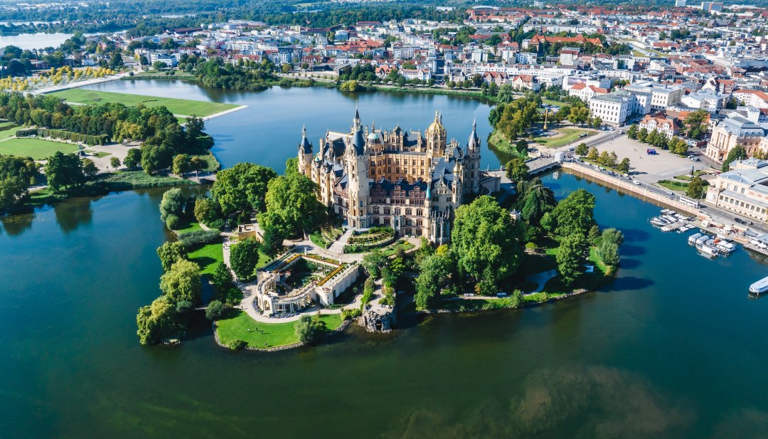 Das Schloss Schwerin aus der Luft im Sommer. Das Schloss steht auf einer kleinen Insel, umgeben von Wasser.