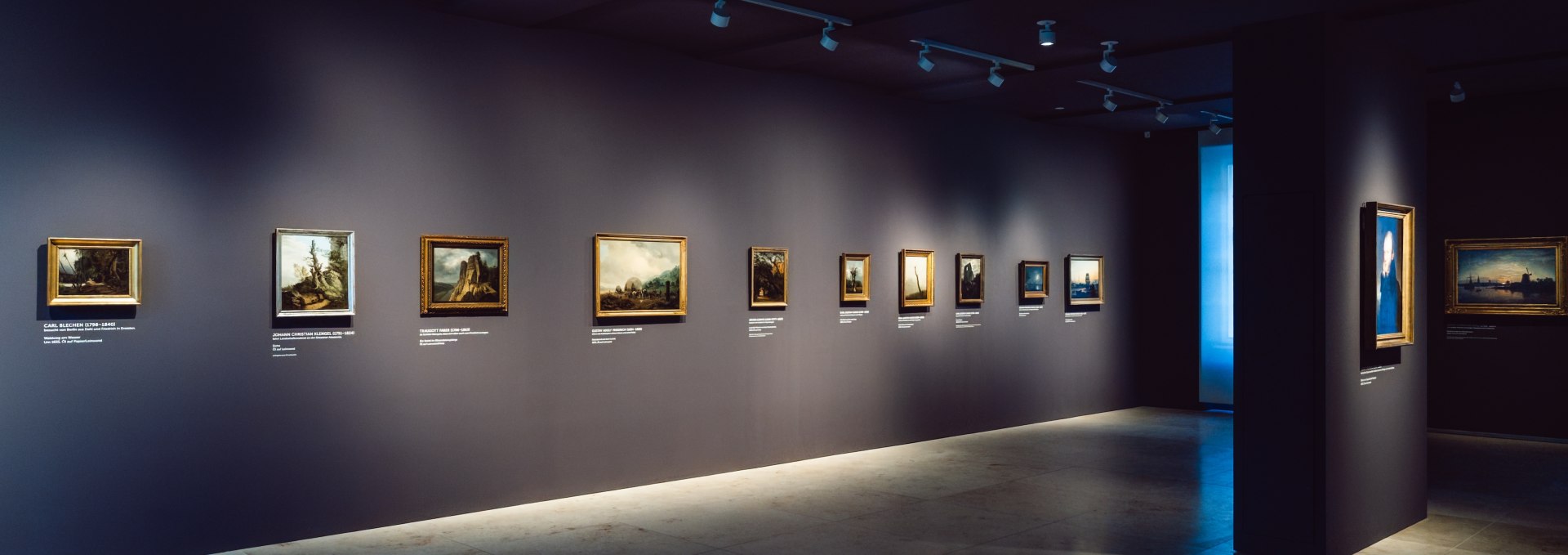Donkere tentoonstellingsruimte met romantische schilderijen op een donkergrijze muur in het Pommers Staatsmuseum in Greifswald.