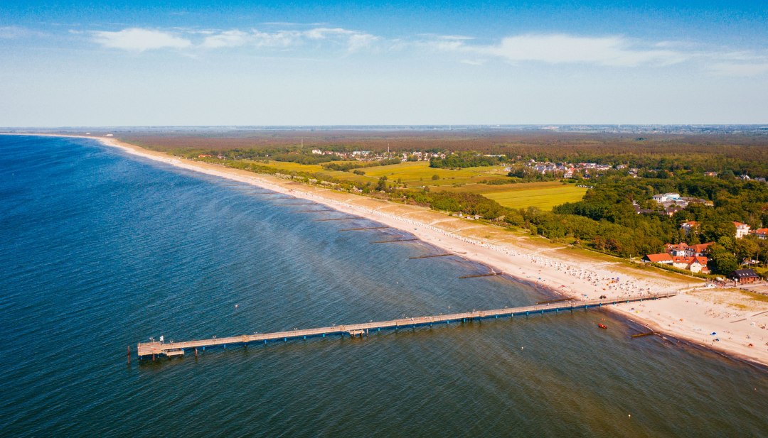 Luchtfoto van de Baltische kust van Graal-Müritz met pier, zandstrand en kustbos. // De pier steekt uit in het turkooisblauwe water, het zandstrand strekt zich kilometers ver uit langs de kust. Graal-Müritz nodigt je uit om te zwemmen, wandelen en diep adem te halen - tussen de Baltische Zee en groene bossen ligt de open ruimte voor vakantiemomenten. // © MV-T/Friedrich Luchtfoto van de Baltische kust van Graal-Müritz met pier, zandstrand en kustbos.