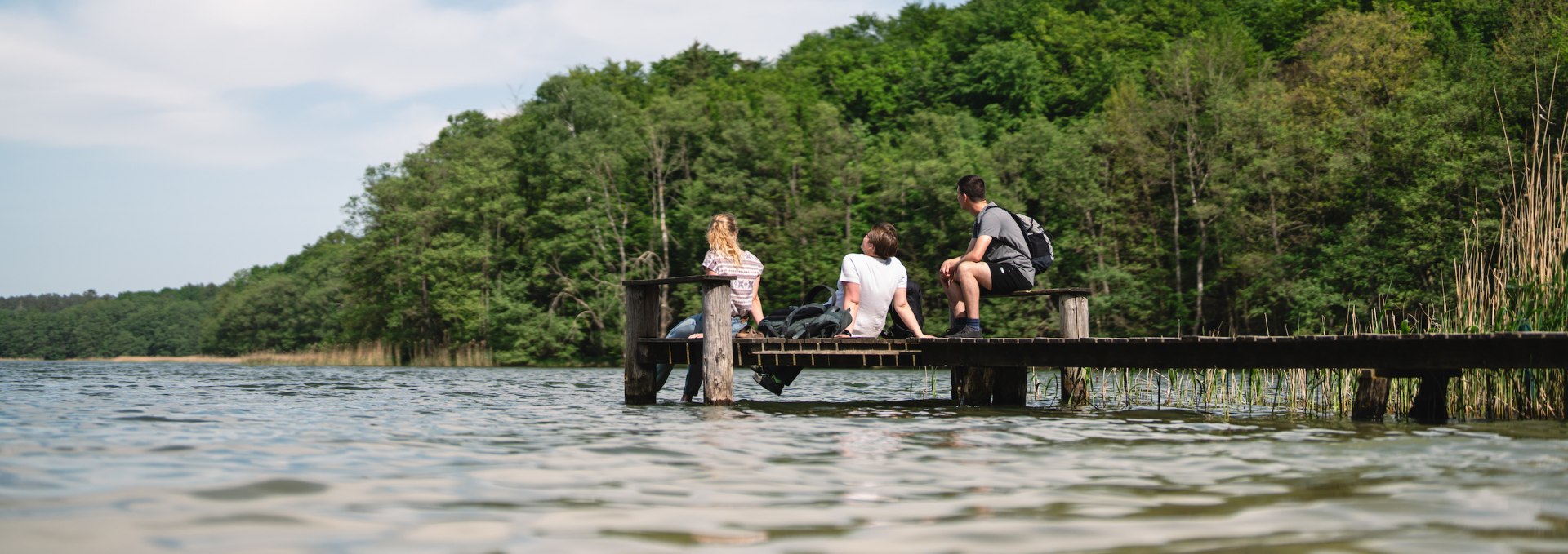 3 Freunde sitzen f&uuml;r eine Pause auf einem Steg am Gro&szlig; Labenzer See bei Friedrichswalde.