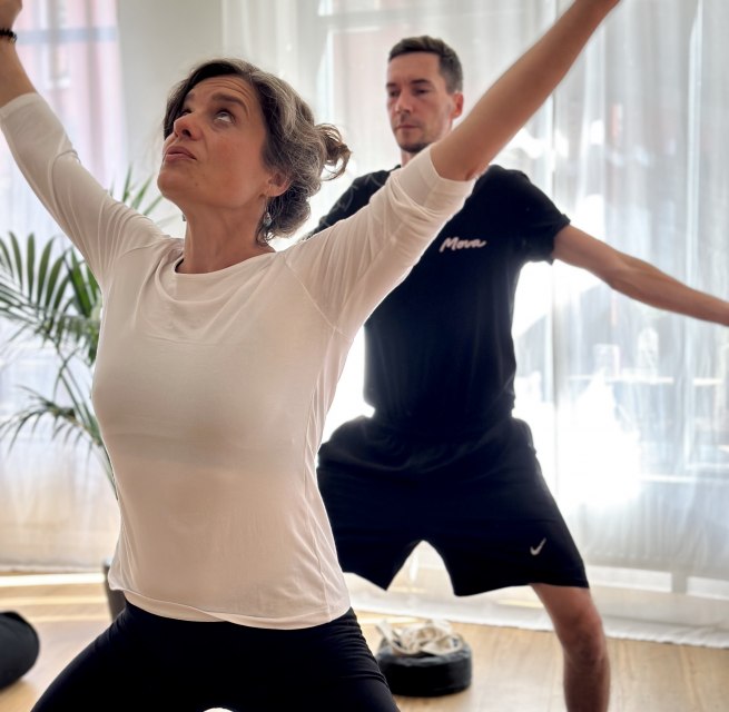 Zwei Personen praktizieren Yoga in einem hellen Studio. Im Vordergrund steht eine Frau in einer kraftvollen stehenden Yoga-Haltung mit erhobenen Armen, im Hintergrund folgt ein Mann derselben Bewegung. Weiches Tageslicht und eine ruhige Atmosphäre unterstreichen Achtsamkeit, Bewegung und Körperbewusstsein. // © MOVA PLACE - Yoga & Co. Studio Zwei Personen praktizieren Yoga in einem hellen Studio. Im Vordergrund steht eine Frau in einer kraftvollen stehenden Yoga-Haltung mit erhobenen Armen, im Hintergrund folgt ein Mann derselben Bewegung. Weiches Tageslicht und eine ruhige Atmosphäre unterstreichen Achtsamkeit, Bewegung und Körperbewusstsein. // © MOVA PLACE - Yoga & Co. Studio