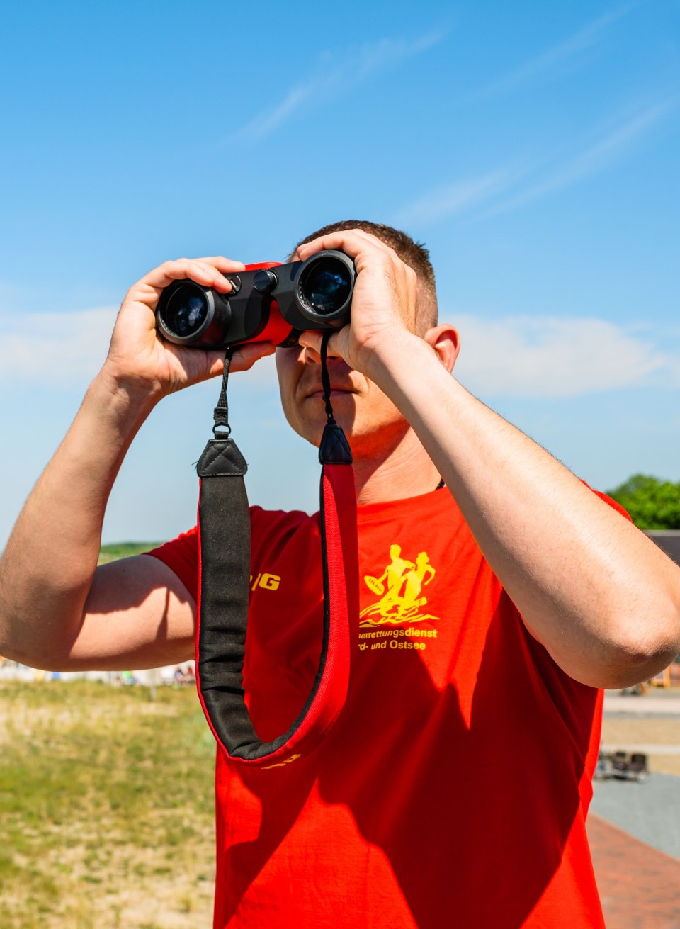 Ein Rettungsschwimmer blickt mit Fernglas &uuml;ber den Strand von Graal-M&uuml;ritz hinweg und beobachtet die Ostsee bei klarem Sommerwetter.