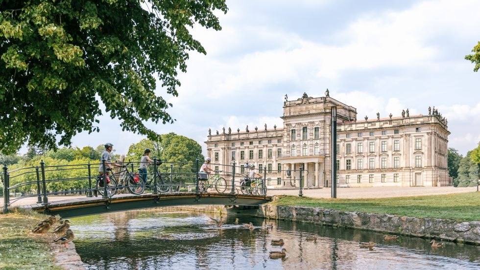 Eine Familie mit Fahrrädern überquert die Brücke mit Kanal am Schloss Ludwigslust // Entdecken Sie die einzigartige Natur und Kultur umweltfreundlich auf abwechslungsreichen Themenradwegen, wie dem Residenzstädte-Rundweg. // © MV-T/Tiemann Eine Familie mit Fahrrädern überquert die Brücke mit Kanal am Schloss Ludwigslust