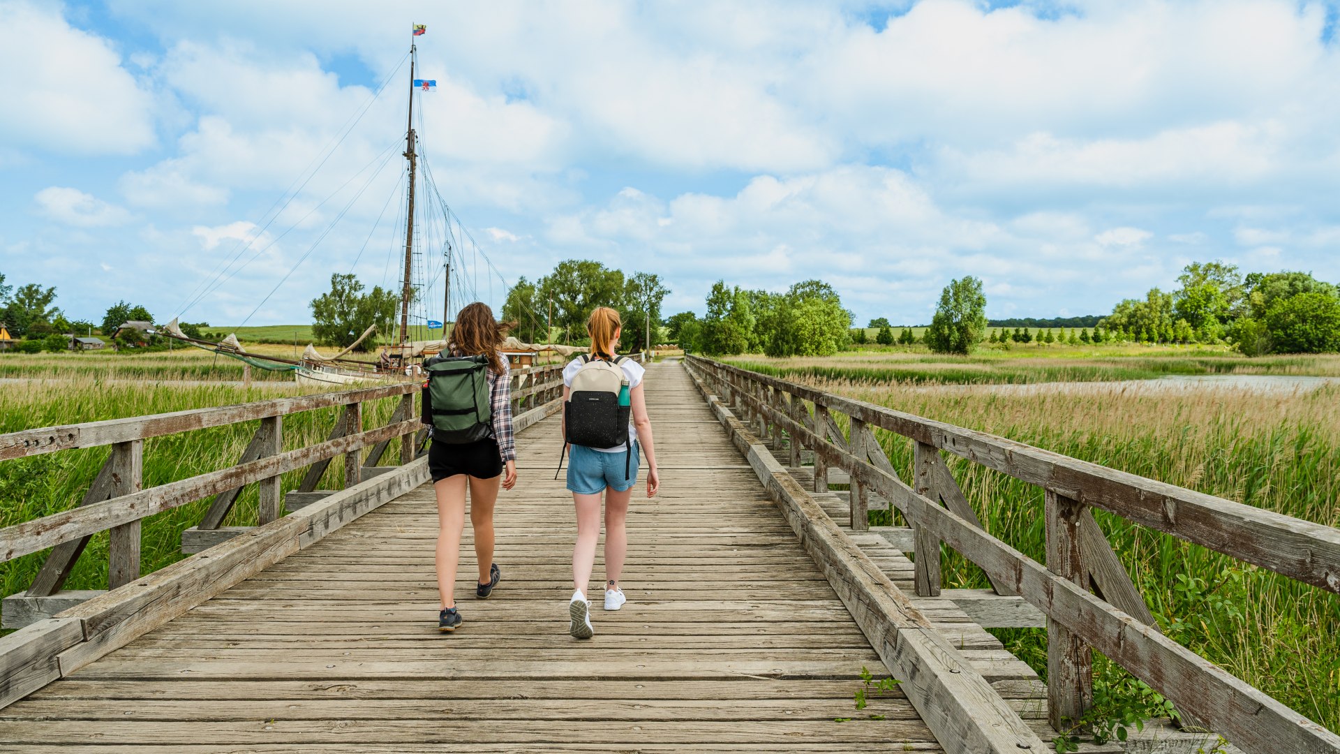 Zwei Frauen wandern über die Holzbrücke Lebbin auf der Insel Rügen // Auf den knarrenden Holzbohlen der Lebbiner Brücke führt der Wanderweg über den Liddower Strom, vorbei am Museumshafen Liddow. // © MV-T/Tiemann Zwei Frauen wandern über die Holzbrücke Lebbin auf der Insel Rügen