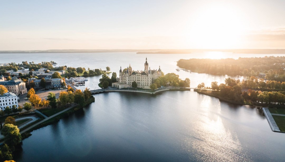 Luchtfoto van het kasteel van Schwerin op een eiland in het meer, omringd door water en bomen bij zonsopgang.