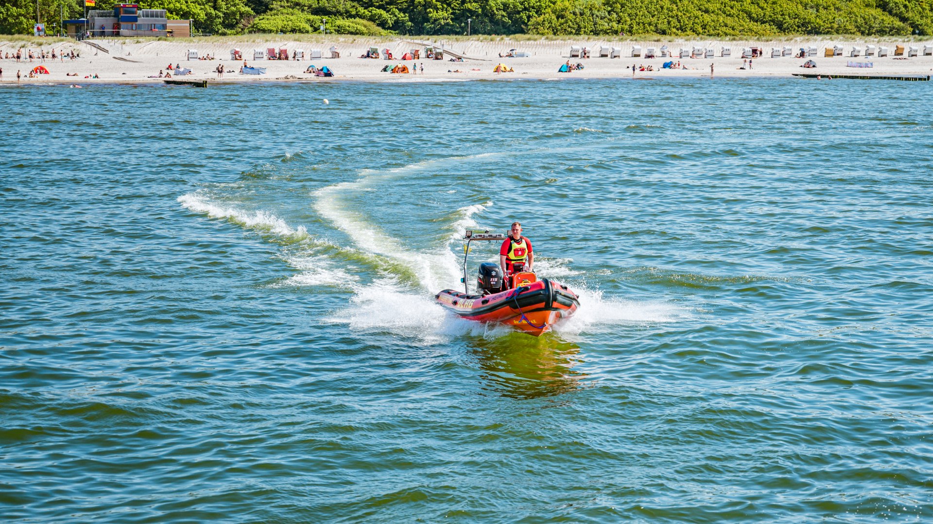 DLRG Motorboot mit Rettungsschwimmer f&auml;hrt auf der Ostsee bei Graal-M&uuml;ritz mit dem Strand im Hintergrund.