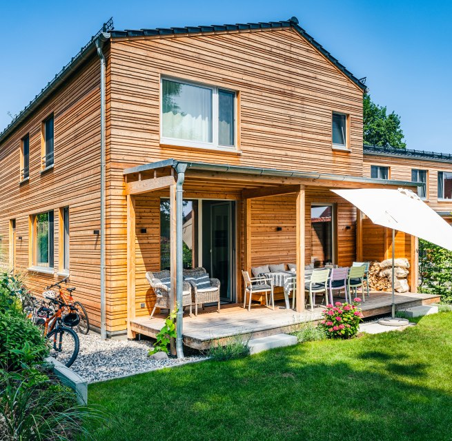 Ein Ferienhaus mit Holzverkleidung und etwas gr&uuml;ner Wiese davor.