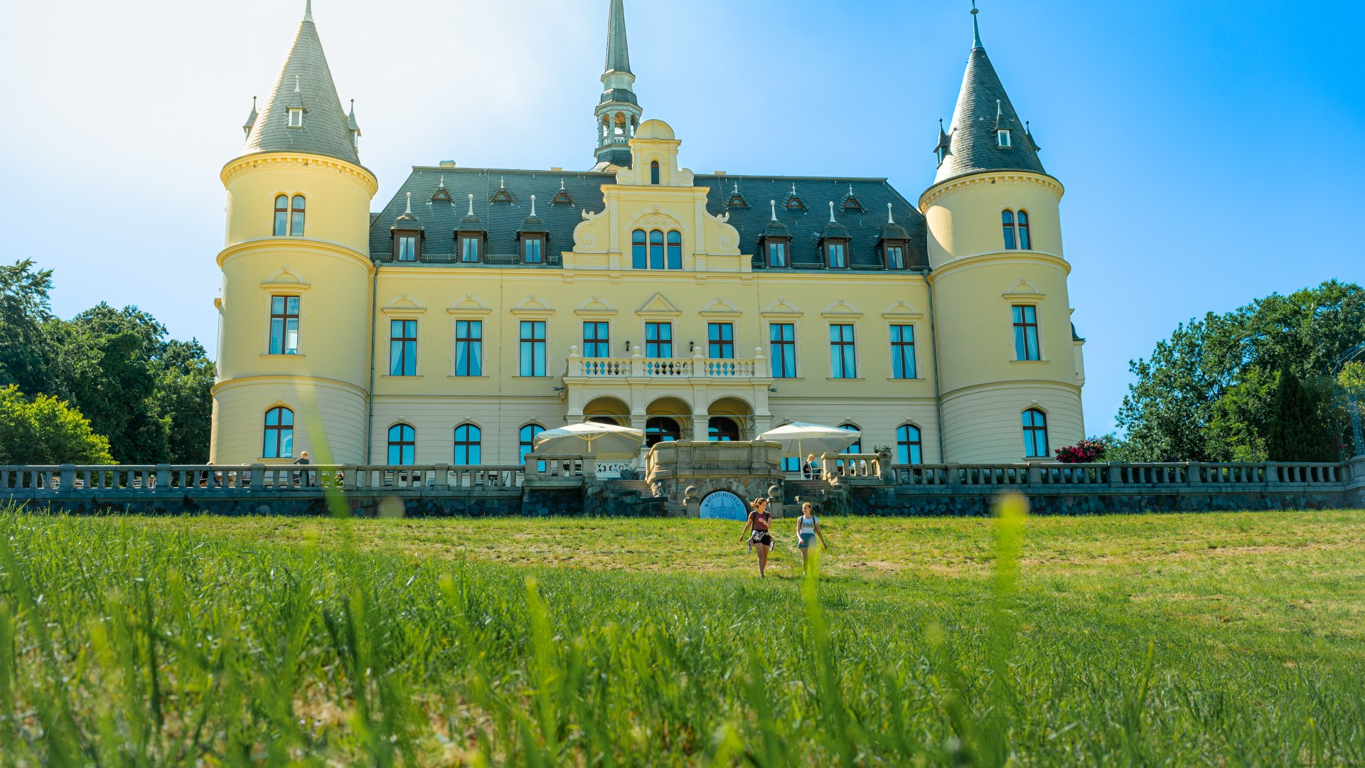 Zwei Frauen spazieren vor dem Schloss Ralswieck // 1896 erbaut diente das Schloss Ralswiek über die Jahre schon als Kasino und Altenheim. Heute befindet sich ein Hotelbetrieb hinter den alten Mauern. // © MV-T/Tiemann Zwei Frauen spazieren vor dem Schloss Ralswieck
