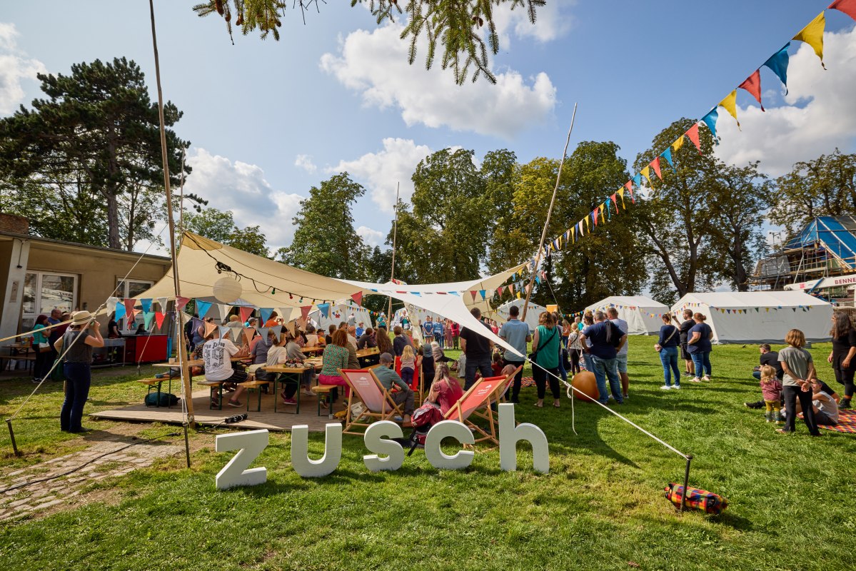 Menschen stehen unter einem mit bunten Wimpeln geschm&uuml;ckten  Sonnensegel, &copy; Oliver Borchert