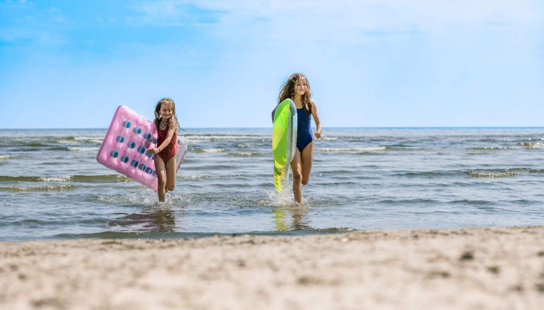 Twee kinderen rennen uit het water het strand op met luchtbedden onder hun armen