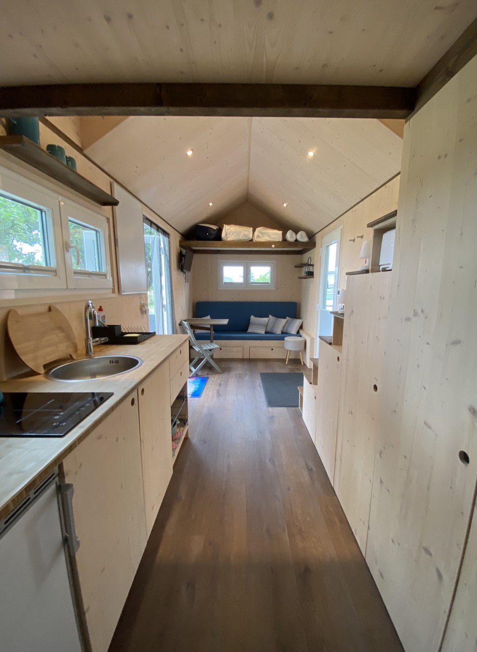 Das Tiny House der Alpaka Idylle mit Ausstattung: Sicht nach drau&szlig;en mit Bett, K&uuml;che und Couch.