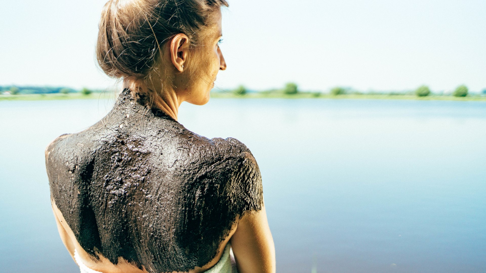 Modderpakking op de rug van een vrouw die in de zon staat met uitzicht op het water.